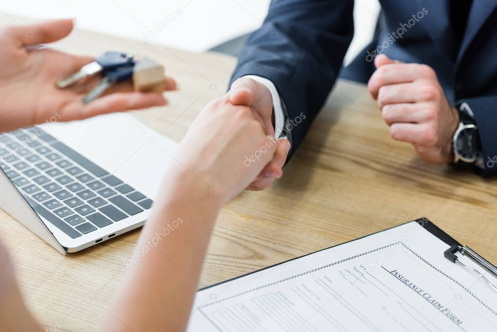 cropped view of woman holding keys in hand and shaking hands with realtor