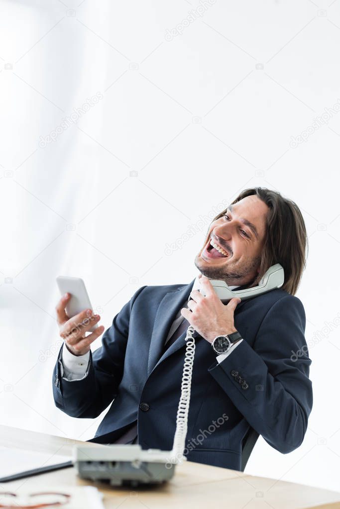 happy handsome businessman talking at telephone, holding smartphone and headset in hands