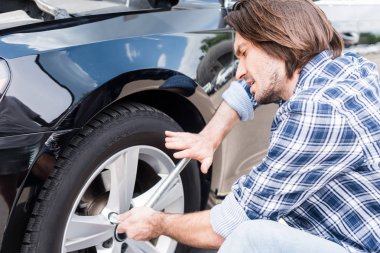 tired man using tool and changing broken wheel on auto, car insurance concept clipart