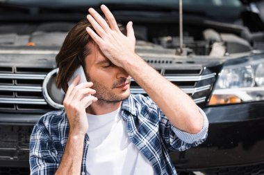 man talking on smartphone near broken auto with open hood, holding hand on head, car insurance concept clipart