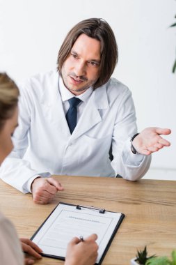 kadın belge imzalarken ve ahşap masanın arkasında otururken doktor hasta ile konuşurken