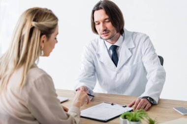 patient sitting with doctor behind wooden table and signing document clipart