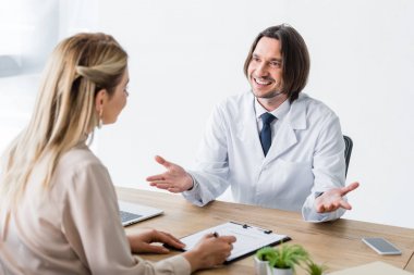 patient sitting with happy doctor behind wooden table and signing document clipart