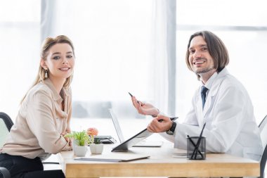 patient and doctor sitting behind wooden table and looking at camera clipart