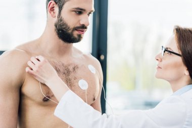 doctor putting electrodes on shirtless sportsman during endurance test