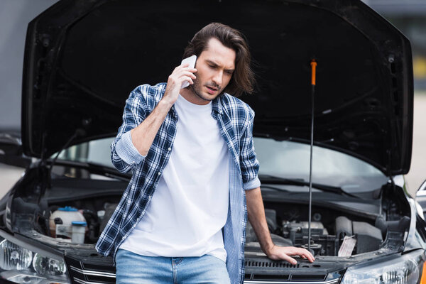 разочарованный человек говорит на смартфоне, стоя рядом со сломанным авто с открытым багажником, концепция страхования автомобиля
