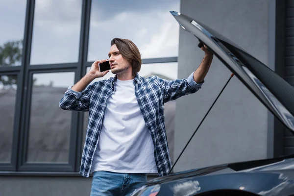 英俊男子在谈智能手机和站在附近的破碎的汽车与开放的后备箱 汽车保险的概念 — 图库照片