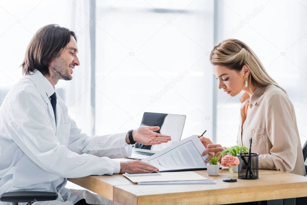 woman signing insurance claim form during appointment with doctor in clinic