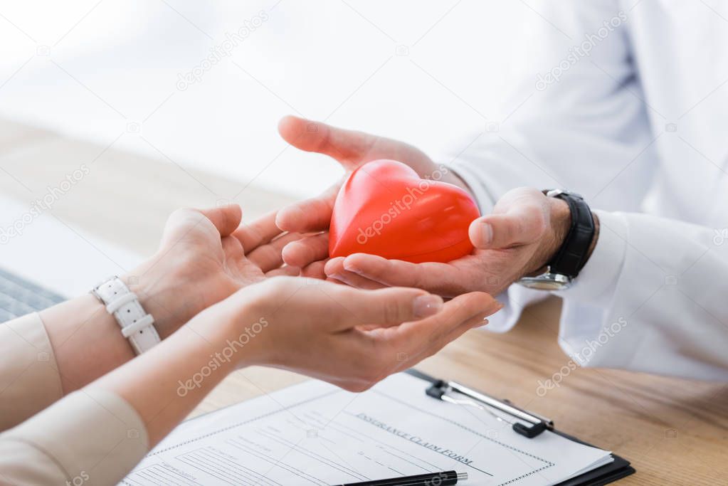 cropped view of  doctor and patient holding red heart in hands, medical insurance concept
