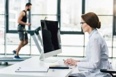 Arzt nutzt Computer, während Sportler beim Ausdauertest im Fitnessstudio auf Laufband laufen