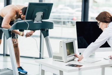 spor salonunda sporcu ile dayanıklılık testi yaparken monitör bakarak doktor