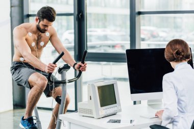 spor salonunda elektrotlar ile sporcu ile dayanıklılık testi yürüten doktor