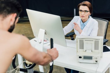 dayanıklılık testi sırasında bilgisayar masasında doktor yakınında eliptik makine üzerinde sporcu eğitimi