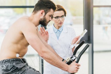 dayanıklılık testi sırasında gömleksiz sporcu yakın dijital tablet gesturing ile doktor
