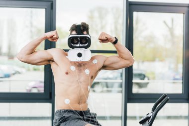 spor salonunda dayanıklılık testi sırasında eliptik üzerinde kasları gösteren elektrotlar ile Sanal gerçeklik kulaklık gömleksiz sporcu