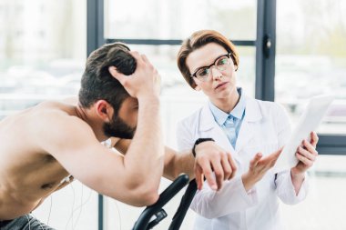 dayanıklılık testi sırasında dijital tablet ile doktor yakınında eliptik makine üzerinde sporcu eğitimi