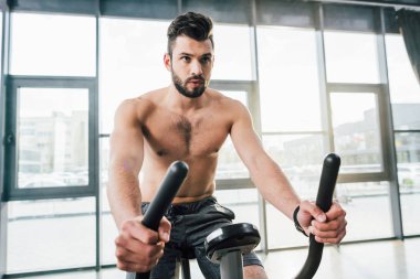 handsome shirtless sportsman training on elliptical machine at gym clipart