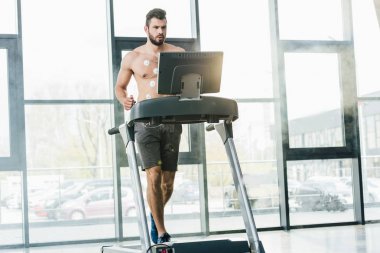 gün ışığı ile spor salonunda dayanıklılık testi sırasında koşu bandı üzerinde çalışan elektrotlar ile yakışıklı sporcu
