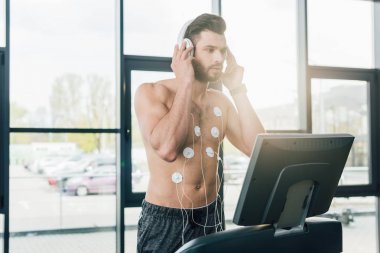 spor salonunda dayanıklılık testi sırasında koşu bandı üzerinde çalışan kulaklık kaslı sporcu