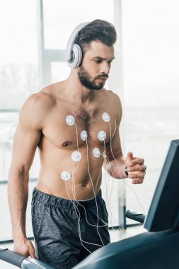 spor salonunda dayanıklılık testi sırasında koşu bandı üzerinde çalışan kulaklık kaslı sporcu