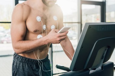 spor salonunda dayanıklılık testi sırasında koşu bandı üzerinde çalışan akıllı telefon ile sporcu nun kırpılmış görünümü