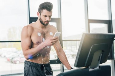 spor salonunda dayanıklılık testi sırasında koşu bandı üzerinde çalışan akıllı telefon ile sporcu