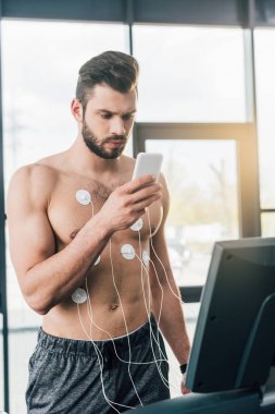 spor salonunda dayanıklılık testi sırasında koşu bandı üzerinde çalışan akıllı telefon ile sporcu