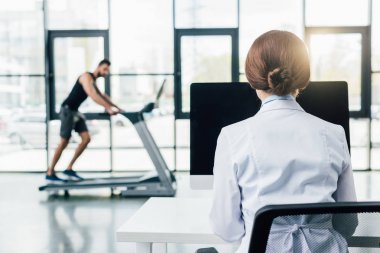 spor salonunda dayanıklılık testi sırasında koşu bandı üzerinde çalışan sporcu ise bilgisayar kullanarak doktor geri görünümü
