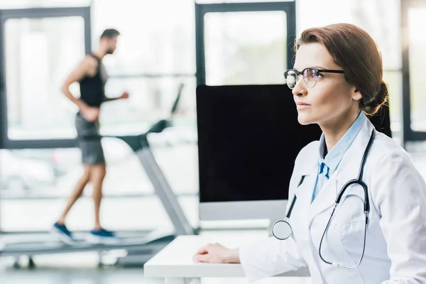 selective focus of doctor near sportsman running on treadmill during endurance test in gym