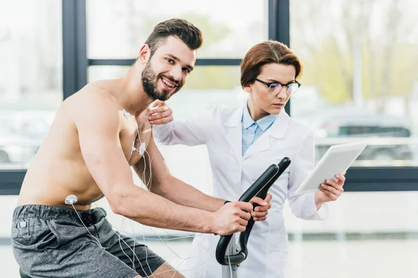 doctor with digital tablet near smiling shirtless sportsman during endurance test