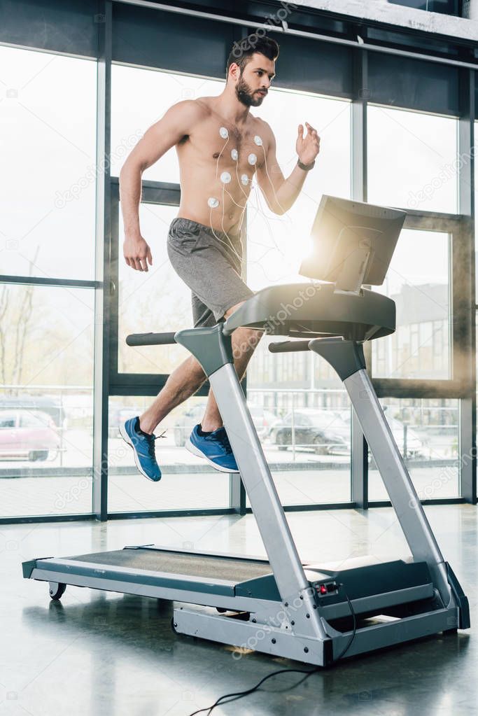 handsome muscular sportsman with electrodes running on treadmill during endurance test in gym