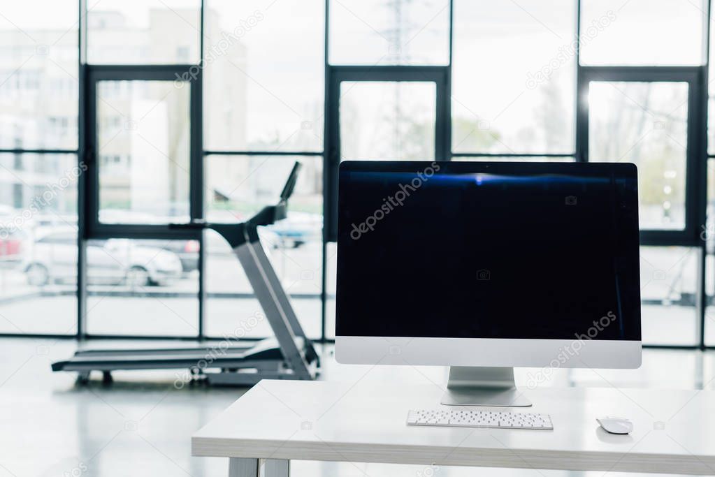 selective focus of computer with blank screen on desk near treadmill at sports center