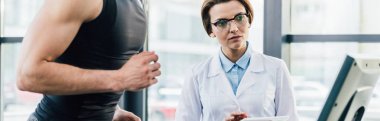 spor salonunda dayanıklılık testi sırasında güzel doktor yakınında koşu bandı üzerinde çalışan sporcunun panoramik atış