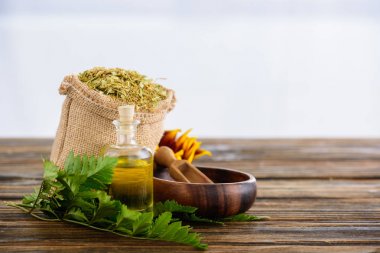 kurutulmuş otlar ile sackcloth çanta, uçucu yağ ile mantarlı şişe, eğrelti otu yaprakları, ahşap kase ve ahşap yüzeyüzerinde spatula