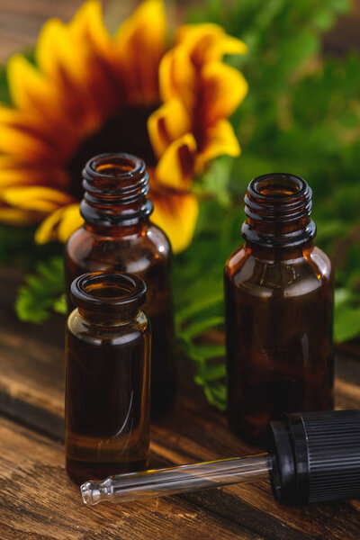 bottles with essential oils, dropper and sunflower on wooden surface