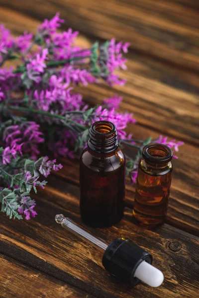 heather plant, bottles with essential oils and dropper on wooden surface
