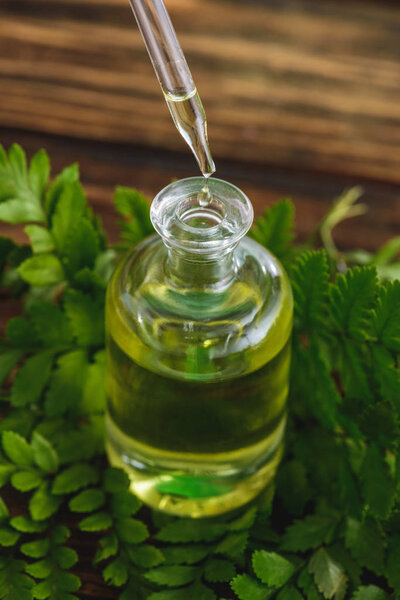 bottle with essential oil, dropper and fern leaves on wooden surface