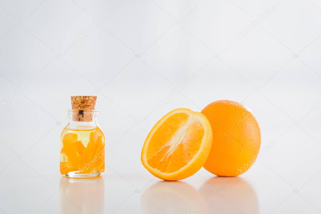 ripe oranges near bottle with essential oil on white background