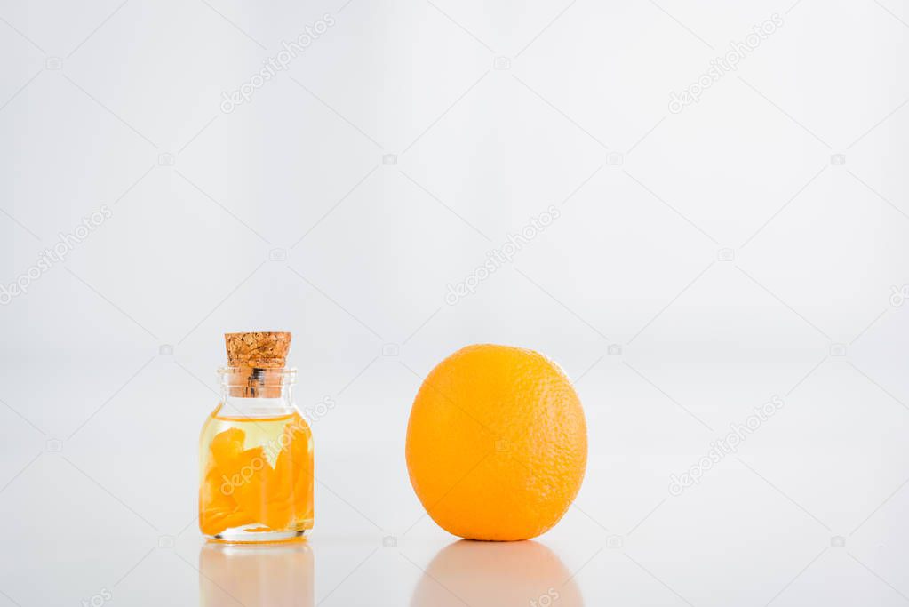 whole orange near corked glass bottle with essential oil on white background