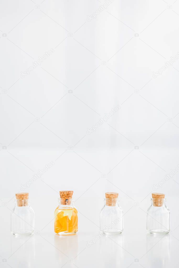 glass corked bottle with orange essential oil near empty bottles on white background with copy space