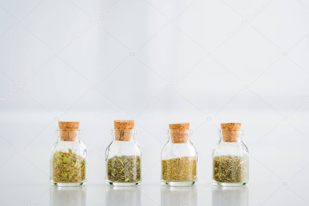 corked jars with dried herbs on white background with copy space