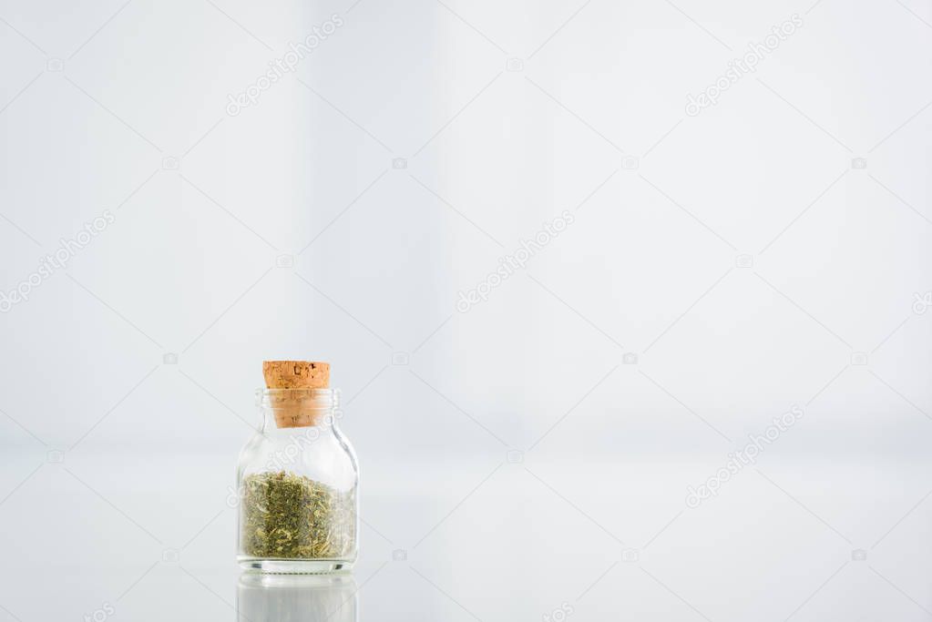 corked jar with dried herbs on white background with copy space