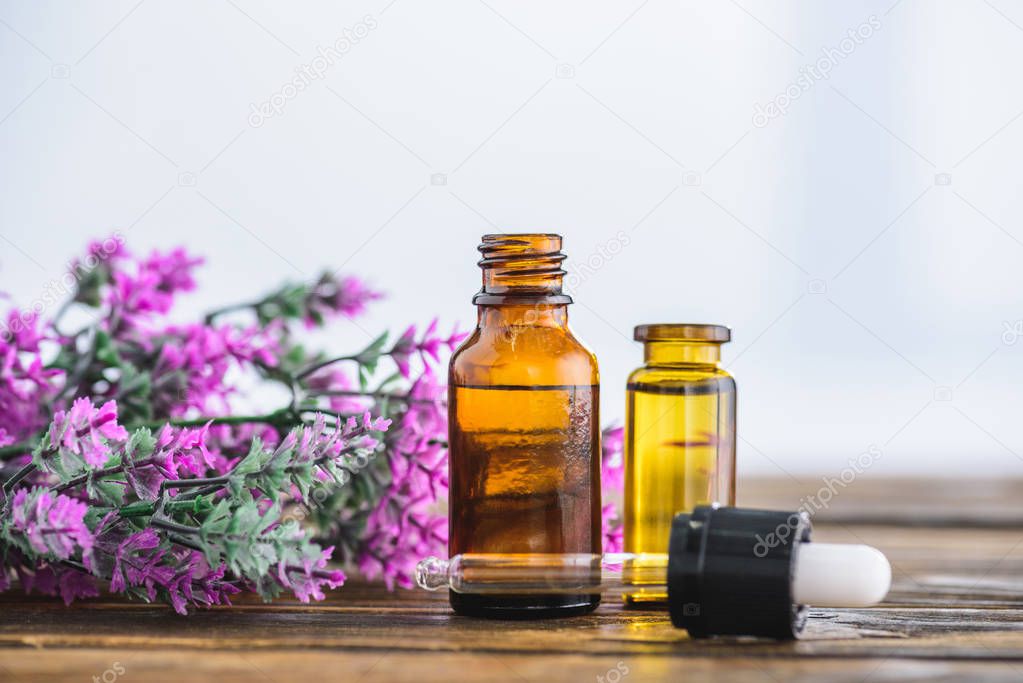 bottles with essential oils, dropper and heather flowers on white background