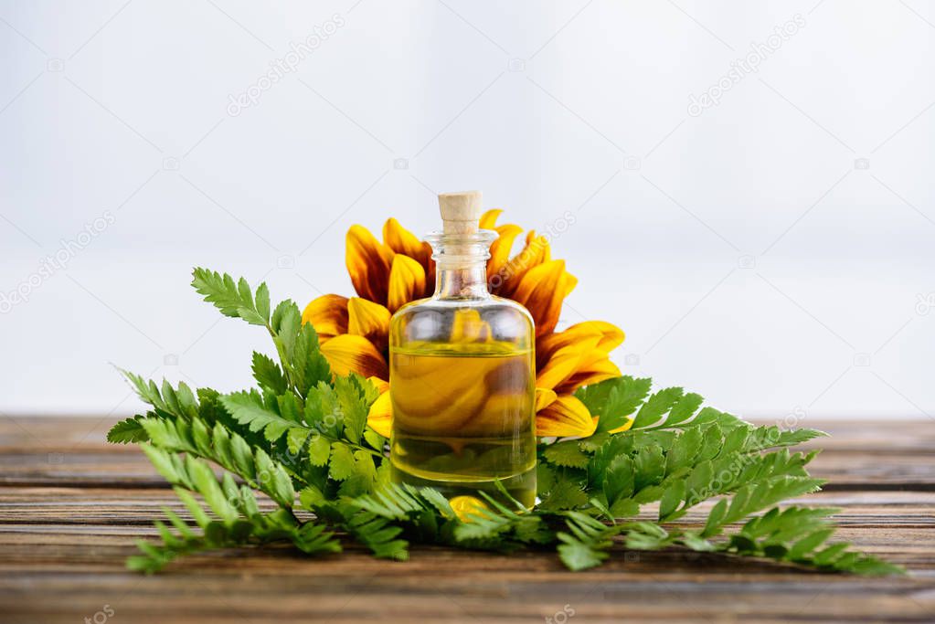 corked bottle with essential oils, fern leaves and sunflower on wooden surface