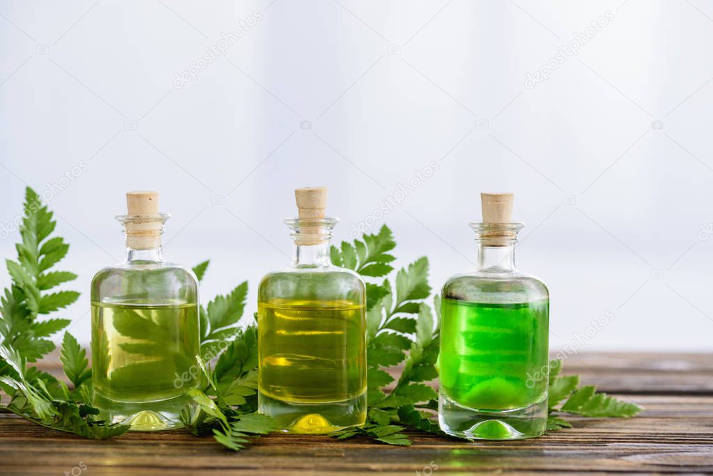 corked bottles with essential oils and fern leaves on white background
