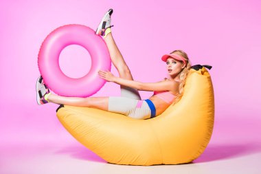 attractive girl on bean bag chair with inflatable swim ring on pink, doll concept clipart