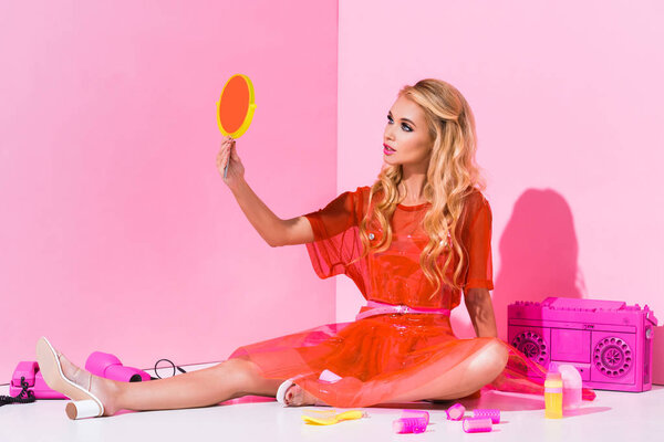 beautiful girl sitting and looking at hand mirror on pink, doll concept