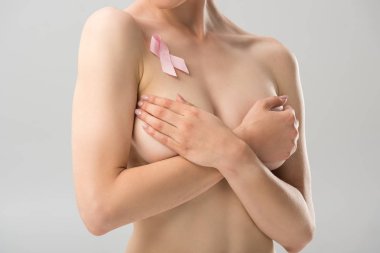 partial view of topless young woman with pink ribbon covering breast isolated on grey clipart