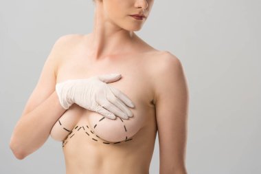 cropped view of woman in latex glove with marks on breast isolated on grey clipart