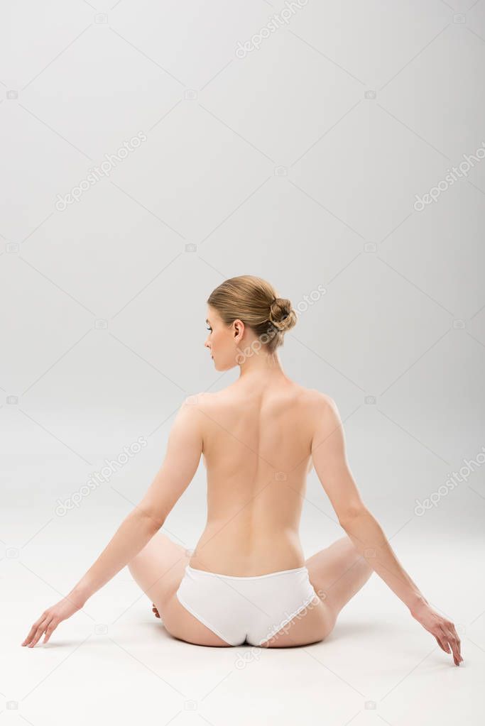 back view of young woman in panties sitting on grey